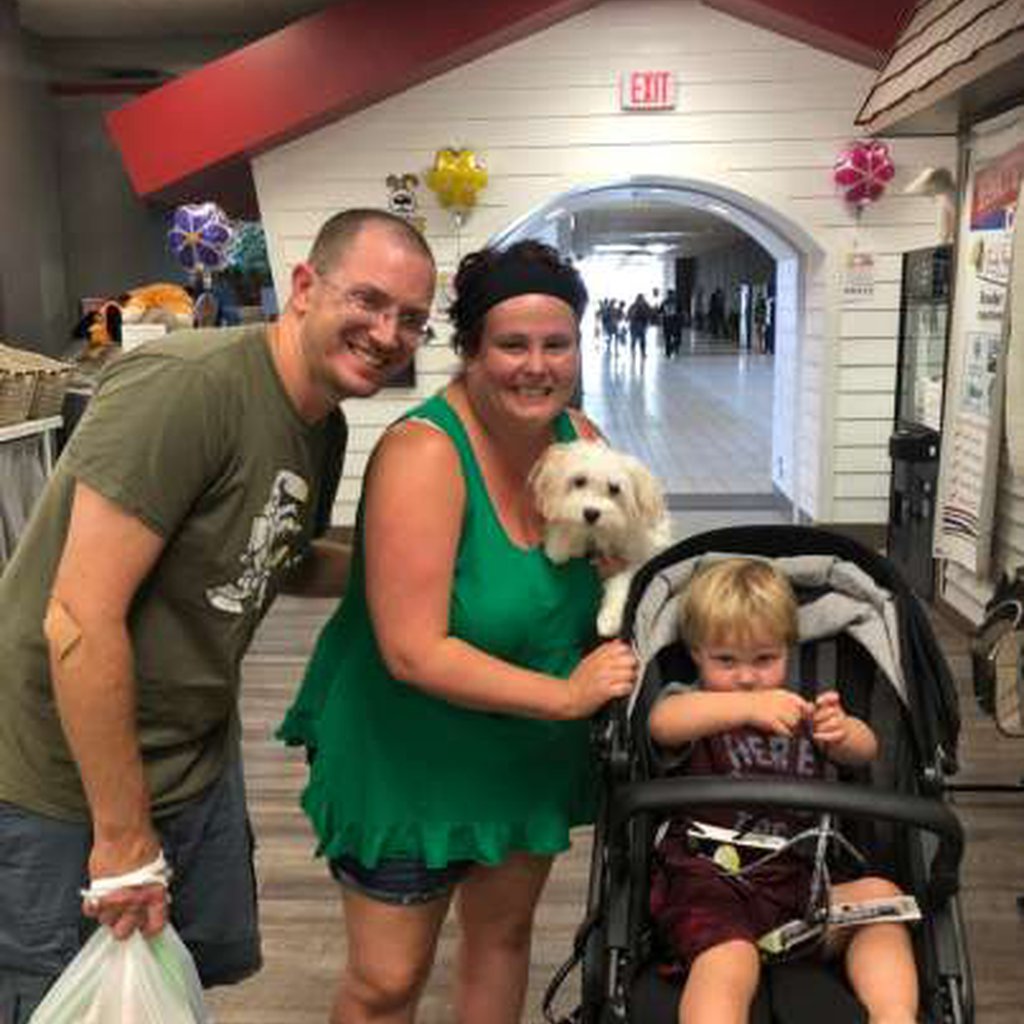 Two adults and a child in a stroller holding a puppy.