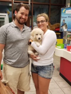 Two people holding a white puppy.