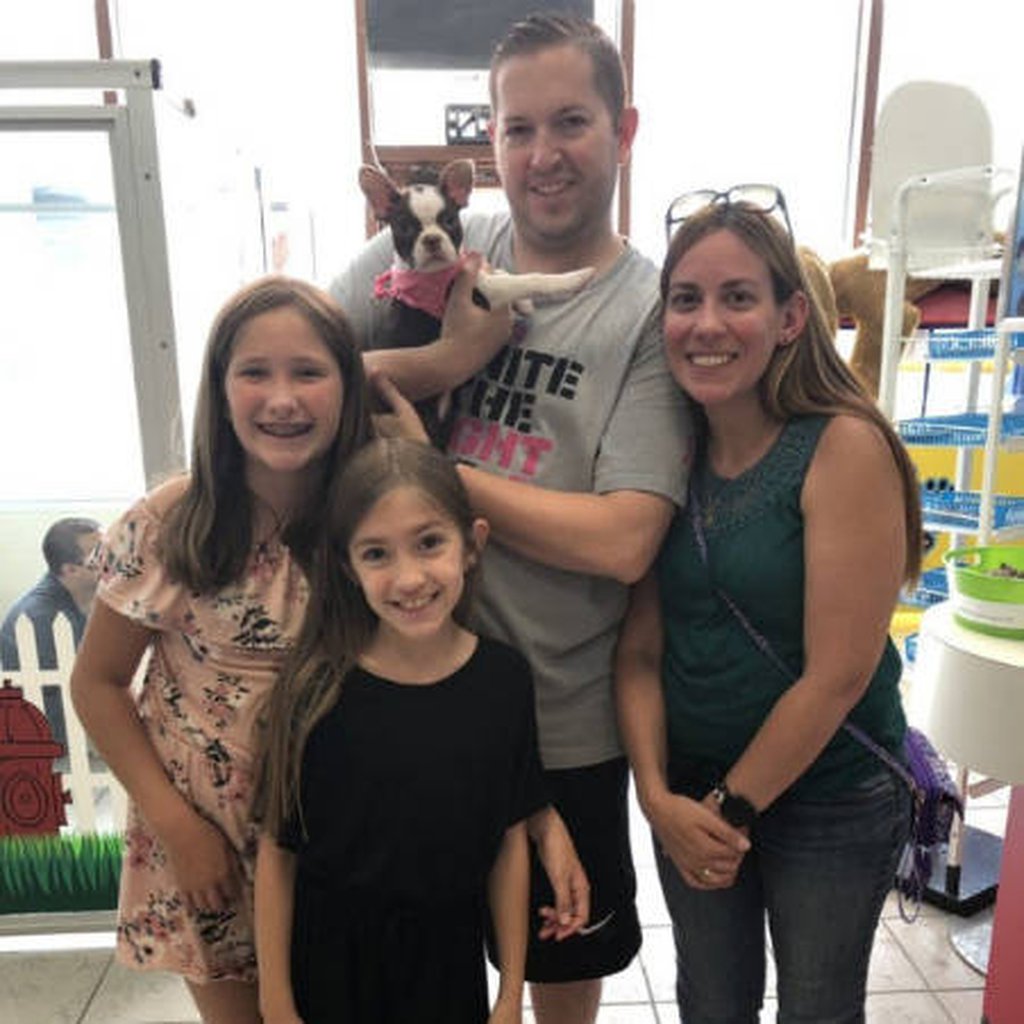 Two adults and two children holding up a black and white puppy.