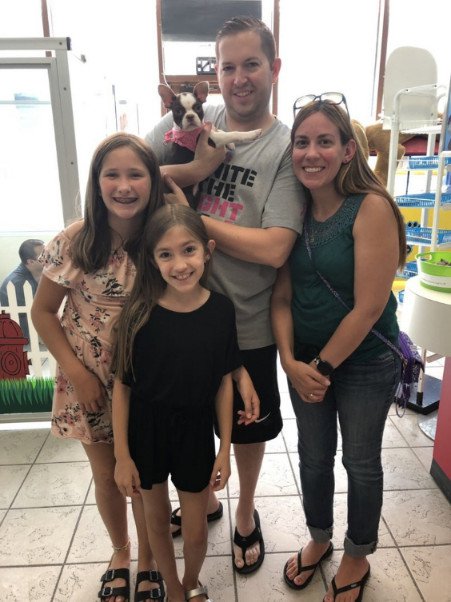 Two adults and two children holding up a black and white puppy.